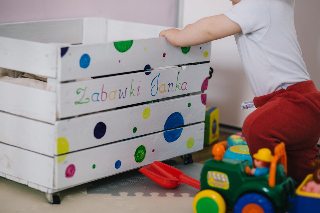 An adorable baby plays near a colorful toy box, surrounded by vibrant toys.