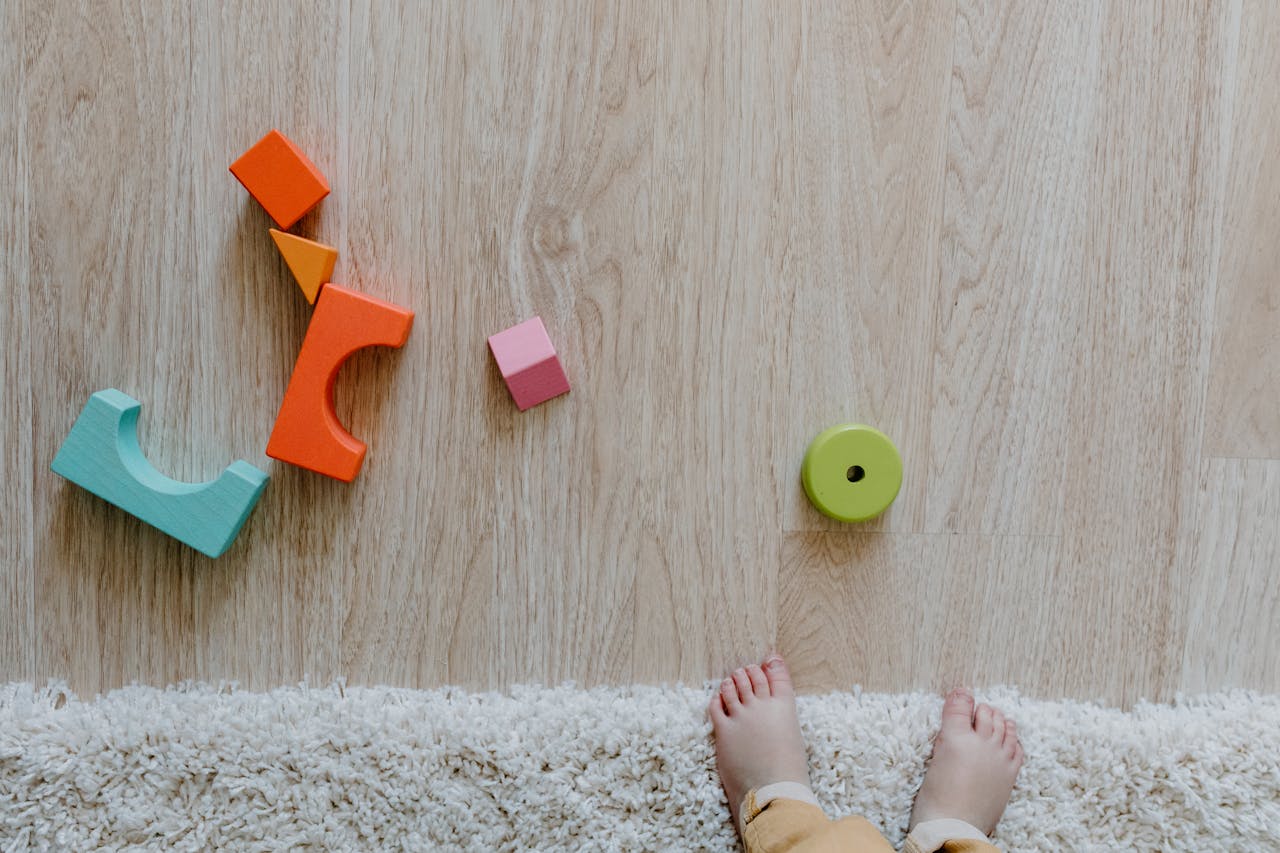 Colorful wooden blocks and baby feet on a carpet and wooden floor, emphasizing child's early playtime.